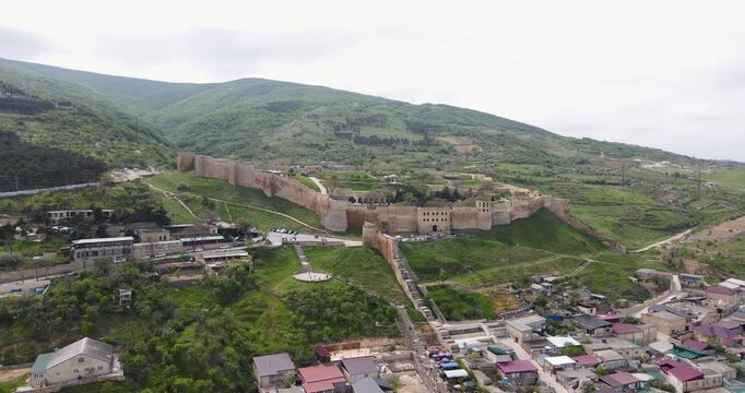 Cinematic aerial orbit shot of the entire ancient Naryn-Kala fortress and old town on green hills in Derbent