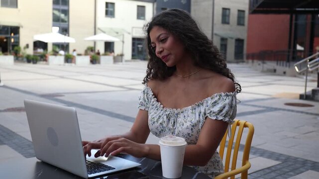 Happy nice woman working on laptop in street cafe.