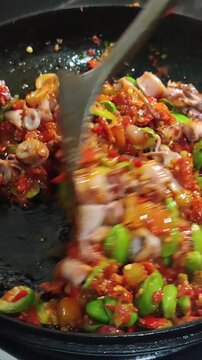 Cooking spicy squid with bitter beans or sambal cumi pete in a wok