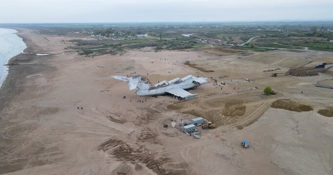 High angle aerial orbit shot of the abandoned Soviet Lun-class ekranoplan on a sandy shore park construction site in Derbent