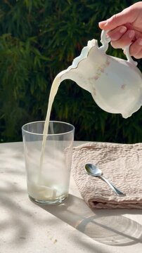 Hot milk poured from ceramic jug into glass at breakfast