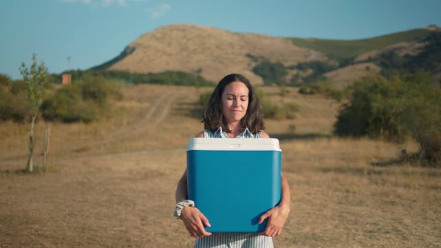 Woman carrying cooler for summer picnic in open countryside