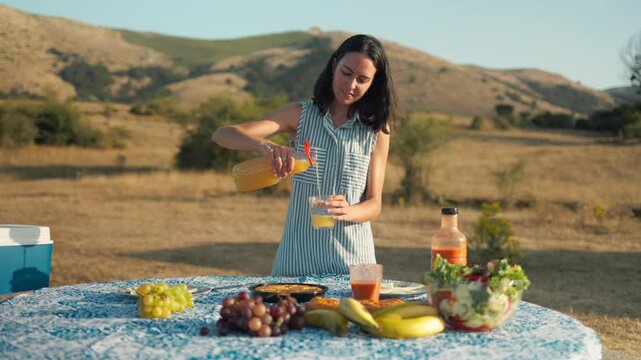Woman pouring fresh juice at summer picnic table outdoors
