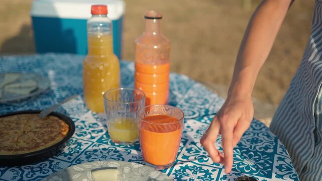 Woman serving gazpacho and juice at summer picnic table