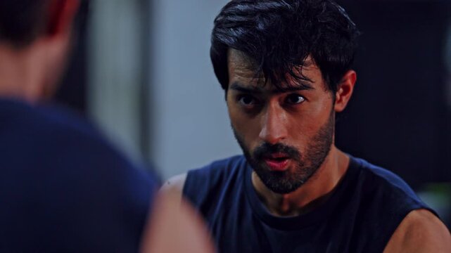 Man portrait mirror reflection beard wet hair sleeveless shirt serious athlete gym training intense gaze after workout indoor fitness scene with moody light focused expression