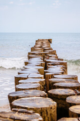 Fototapeta premium Weathered wooden groynes extending into the calm sea at sandy beach