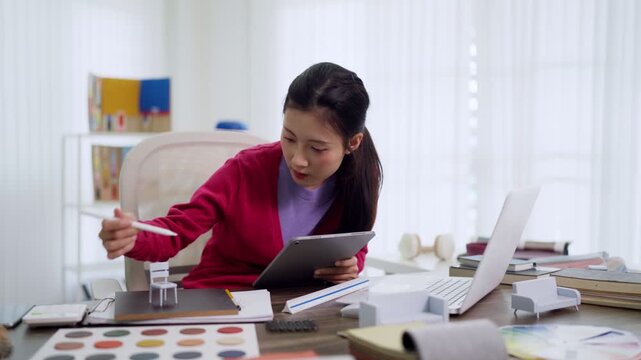 Asian furniture designer reviewing tablet digital plans color samples working creatively product development bright home office creative professional workspace