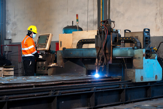 Industrial factory worker operating automated laser metal cutter machine, engineer technician control panel automated laser metal cutter machine heavy industry steel manufacturing factory production