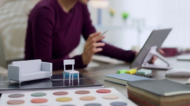 interior designer selecting furniture color swatches using digital tablet with miniature sofa chair samples working on creative project at home office studio