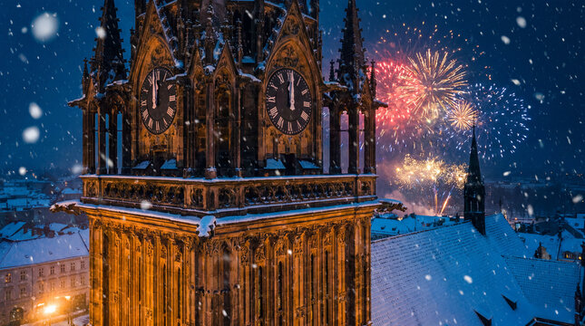 Gothic clock tower at midnight with fireworks over snowy city skyline