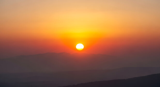 Setting sun over mountainous terrain warm orange and red atmospheric photo sunset