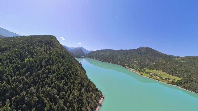 scenic aerial footage pilot point of view, of turquoise lake in a narrow valley of french alps under blue sky and reflection of the moutain on the calm waters