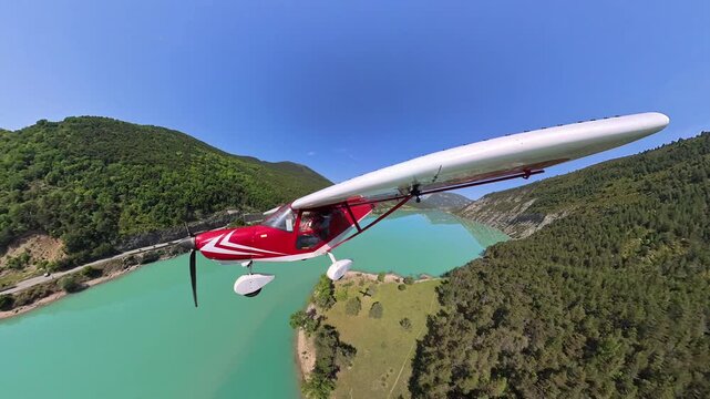 aerial footage, dynamic selfportrait of light airplane flying at low altitude over turquoise lake in a norrow valley of the french alps under blue sky 