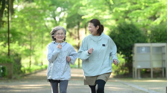 [スローモーション]新緑背景でシニア女性と娘世代の女性が公園でランニングやウォーキング(歩く,走る)のスポーツや運動を楽しむ健康的な笑顔のイメージの動画