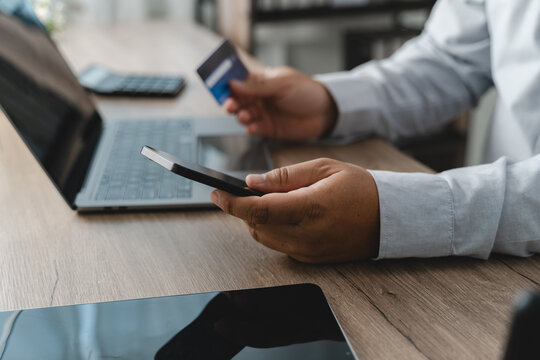 Person holding a smartphone and credit card while using a laptop for mobile banking, online payment authorization and digital financial transaction management in a cashless environment.