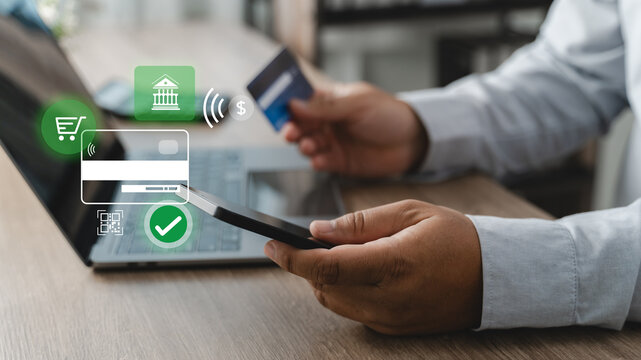 Person using a smartphone, credit card and laptop for online banking money transfer, digital payment authorization and secure financial transaction process in a modern cashless banking environment.