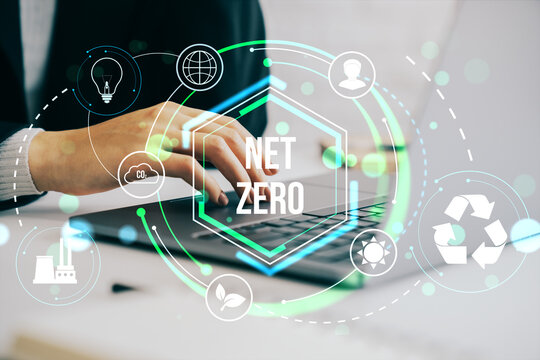 Business person typing on laptop with glowing net zero sustainability icons, digital eco symbols and green energy graphics on bright background.