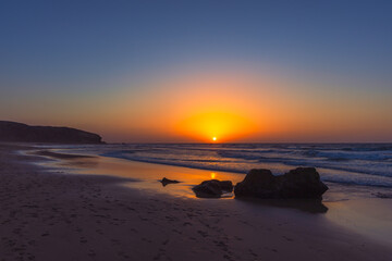 Obraz premium Vibrant Golden Sunset Over Atlantic Ocean Horizon From Sandy Beach With Rocks