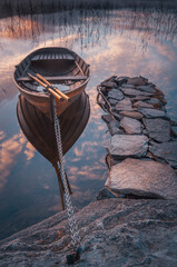 Obraz premium Row boat on still lake with stones and reflections at sunset in Sweden