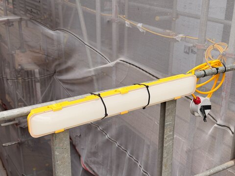 Temporary site light fixed to scaffold rail on construction facade