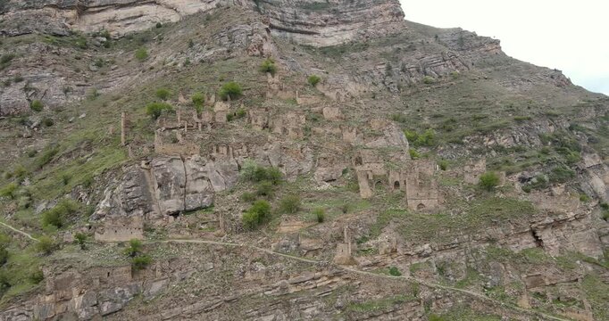 Cinematic aerial pull-away shot of the ancient abandoned stone village ruins terraced on a steep mountain slope in Kahib, Dagestan