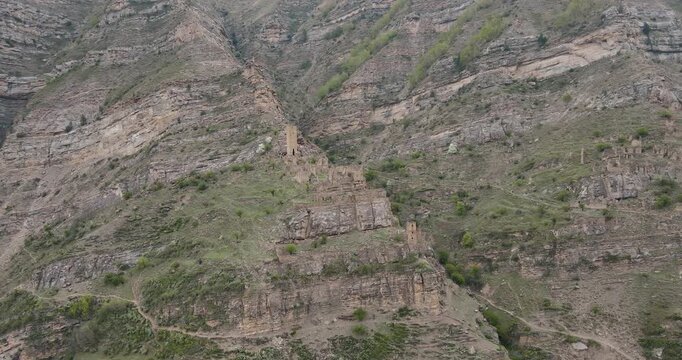 Cinematic panoramic aerial orbit shot of ancient defensive stone watchtowers and village ruins in a steep mountain gorge of Kahib