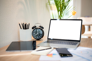 Fototapeta premium Laptop Mockup with Blank White Screen and Alarm Clock on Wooden Desk in Bright Cafe Workspace