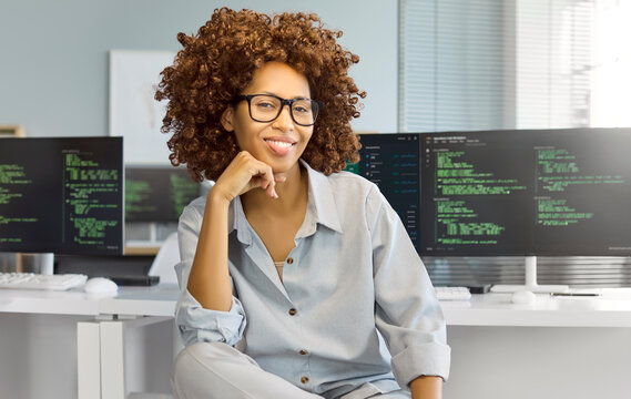 Woman programmer developer coder coding at computer office. Smiling professional in glasses works by monitors, showing software skill in a technology office. Clear tech career concept now.