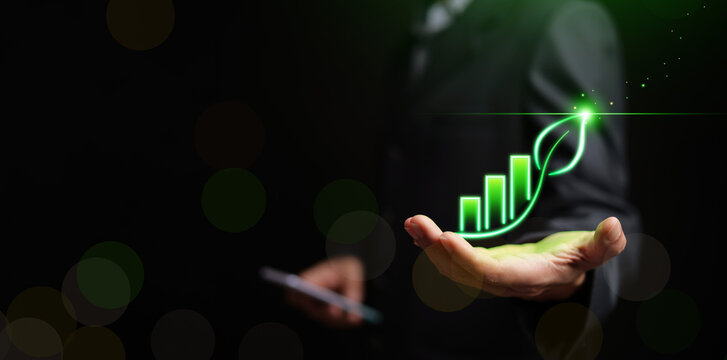 Business professional with glowing green growth chart shaped as a leaf above an open hand. ESG performance, sustainable growth, green investment, climate responsibility, and corporate sustainability.