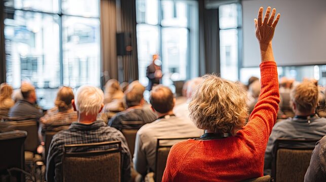 Audience member raises hand for question during presentation in large room