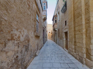 Obraz premium Narrow cobblestone alley between traditional old limestone residential houses and balconies in Mdina, Malta