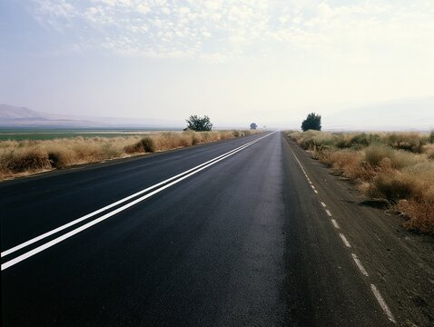Rural Road Stretching into the Distance with Double Lane Markings, Flanked by Dry Grass and Hills