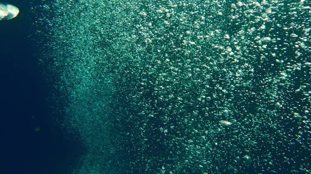 Top view of an endless stream of air bubbles rising upward from deep sea against blue water. Natural underwater background with air bubbles popping up from depths, concept of group scuba diving