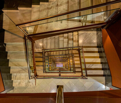 Modern and Elegant interior staircase seen from above featuring metal and glass structure, symmetrical lines and geometric marble pattern