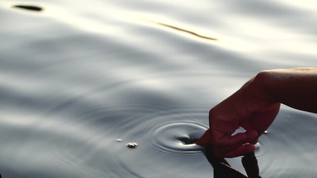 Calm Nature Touch Human hand gently dips fingers into serene water, creating beautiful ripples and reflections at sunset