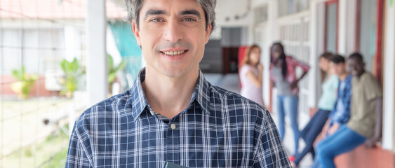 Obraz premium Happy teacher standing in the school hallway, group of students behind him