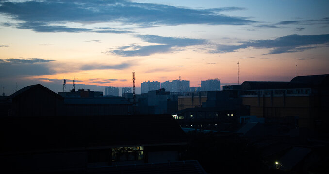 Urban city skyline at twilight with colorful sunset clouds and silhouetted buildings, capturing a peaceful evening atmosphere in a modern metropolitan landscape