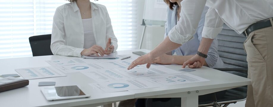Business team collaborating in an office meeting, reviewing charts, reports and market data on tablets and paper while strategizing, analyzing finances and planning next steps