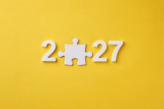Year 2027 concept, white numbers and a puzzle piece on a yellow background