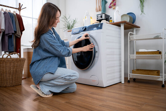 Young Asian woman closing the door of a front-loading washing machine before starting a laundry cycle