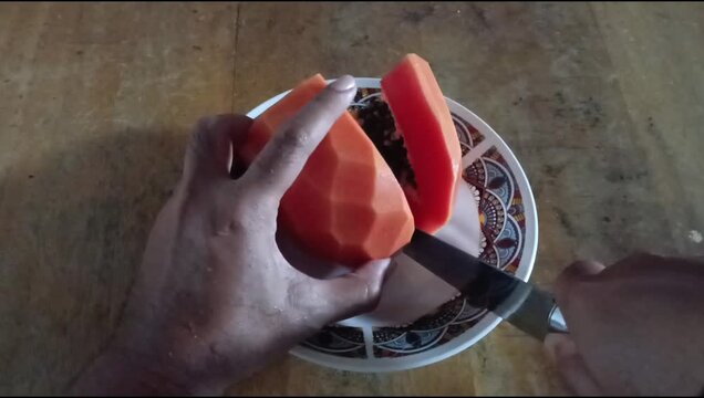 Peeled papaya on a ceramic plate, cut manually with a kitchen knife on a wooden table, fruit is good for digestion
