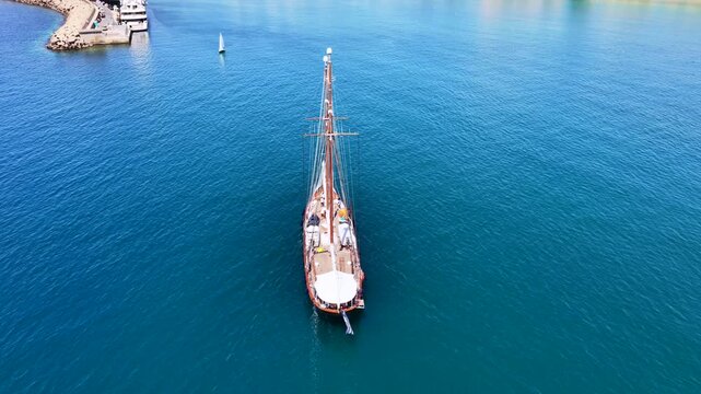 Aerial drone cinematic video of classic sailing wooden ship cruising in low speed near marina and port of Zea or Pasalimani, Piraeus, Attica, Greece