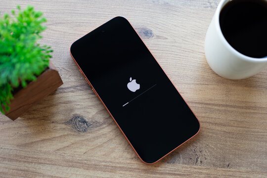 Mobile Apple iPhone 17 Pro Max Cosmic Orange showing the Apple logo on a black boot screen, on desk with coffee in the background