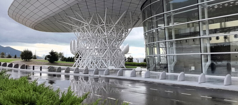 Modern airport terminal exterior with unique white lattice column and curved glass facade on a rainy day. Gelendzhik Airport.