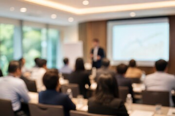 Fototapeta premium Blurred view of a speaker presenting to an audience in a conference room with a projection screen displaying a chart.