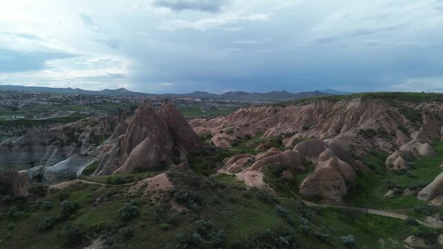 4K drone hovers at 50m before Rose Valley's volcanic peaks in Cappadocia, capturing the striking contrast between light grey summits and warm reddish highlands. Raw, unedited footage.