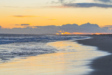 Fototapeta premium Early morning sunlight peeks through clouds, casting golden reflections on the wet sand
