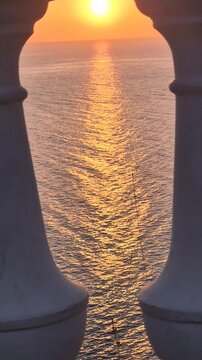 Sunset ocean horizon viewed through white stone balusters on a balcony during golden hour for a serene atmosphere