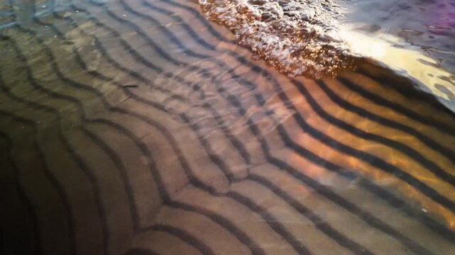 Golden sunset wave slow motion, cinematic sea water ripple, macro sand patterns underwater, ocean beach tide reflection, background travel tourism recreation, evening sunlight over fluid current.