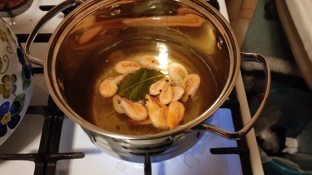 Cooking shrimp with bay leaf in stainless steel pot on gas stove, top view